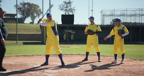 Batter Preparing to Swing with Teammates in Yellow Uniforms on Sunny Baseball Field