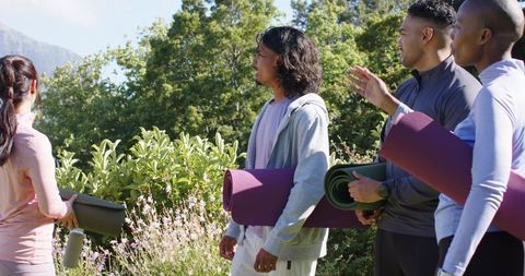 African american friends carrying yoga mats in garden preparing outdoor wellness session