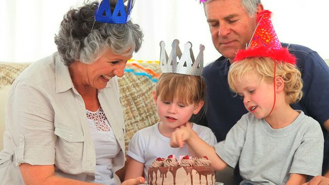 This scene captures a joyful family gathering where grandparents and their grandchildren celebrate a birthday with an indulgent chocolate cake. Each family member wears colorful party hats, adding a festive touch to the occasion. This delightful moment is perfect for use in family-oriented advertisements, birthday greeting cards, or articles focused on family values and celebrations.