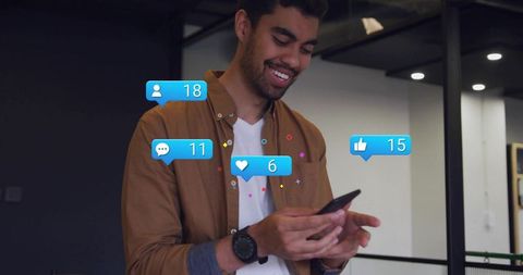 Smiling young man using smartphone in coworking space receiving social media notifications