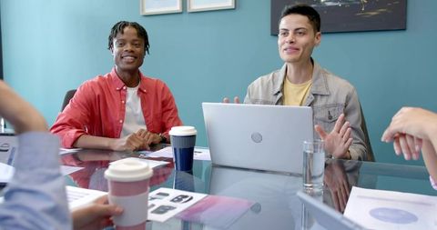 Young Professionals Discussing Project Around Glass Conference Table With Laptop and Coffee