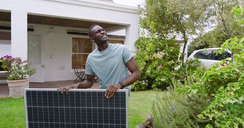 Man Holding Solar Panel Outdoors Near Modern Home