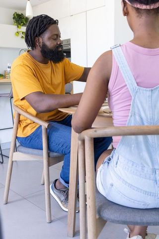 African father and teenage daughter sharing conversation at modern kitchen table