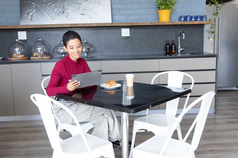 Young african american woman working on tablet at modern kitchenette with coffee and pastry