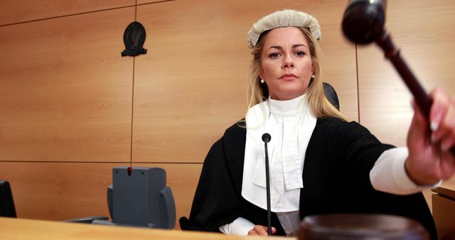 A middle-aged Caucasian woman dressed as a judge is wielding a gavel in a courtroom, with copy space. Her authoritative gesture captures a moment of legal decision-making, emphasizing the gravity of judicial proceedings.