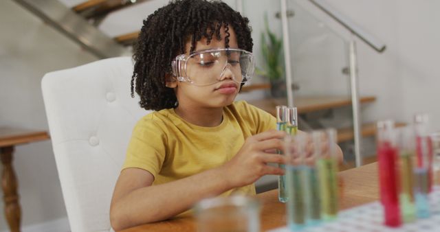 Young boy wearing safety goggles conducting science experiment at home with test tubes. Engaging in STEM learning activities, this image is perfect for educational purposes, blogs about homeschooling, science-related articles, and publications on children's educational activities.