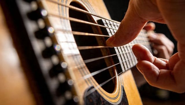 Plucking acoustic guitar strings close-up showing rosette fretboard woodgrain hand