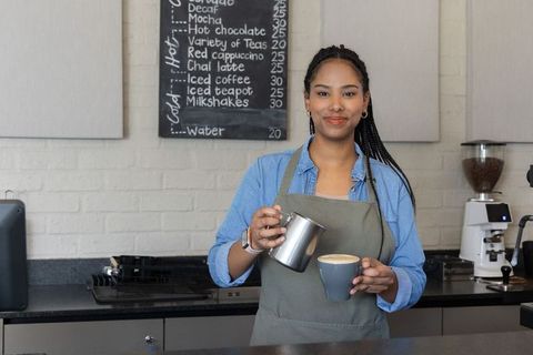 African american barista pouring latte into cup behind modern café counter, smiling
