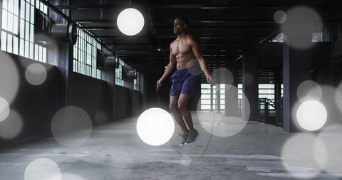Shirtless male athlete jumping rope midair in industrial warehouse cinematic cardio training