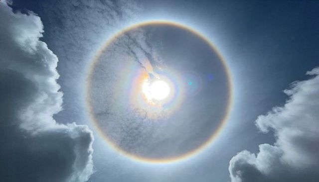 Dramatic circumsolar halo around sun with iridescent rainbow corona and cumulus clouds