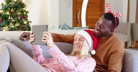 Joyful Diverse Couple Watching Christmas Movie on Tablet