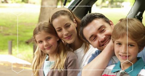 Family of four leaning together in suv tailgate at park, bonding and smiling