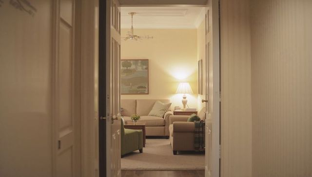 Open doorway framing beige living room with glowing lamp, sofa, armchair and warm ambiance