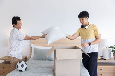 Asian father and son packing pillows during moving day in minimalist soft neutral bedroom