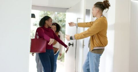Diverse Friends Entering Home While Host Welcoming at Sunlit Doorway