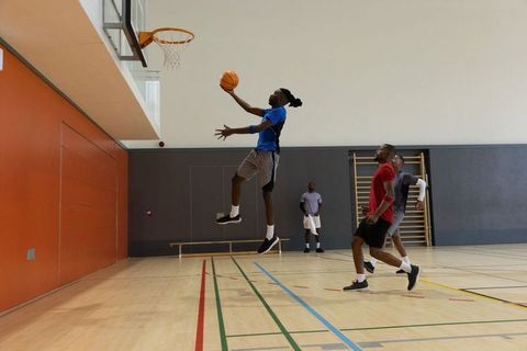 Dynamic basketball layup action with jumping player and teammates practicing in indoor gym