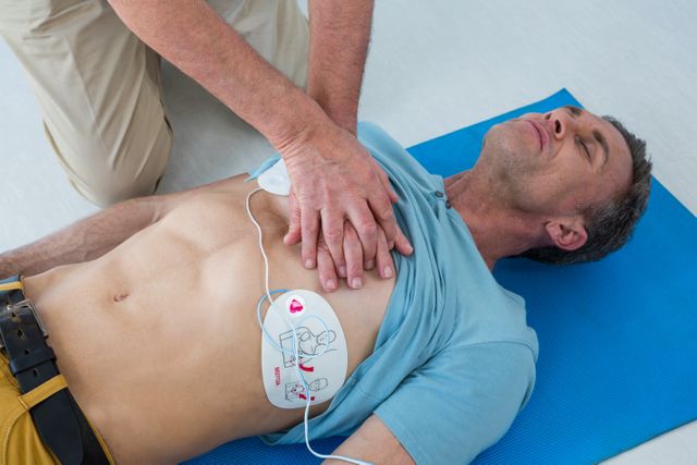 Paramedic performing CPR on patient using an AED in a clinical setting. Useful for illustrating emergency medical procedures, first aid training, healthcare services, and life-saving techniques. Ideal for educational materials, medical training programs, and healthcare awareness campaigns.