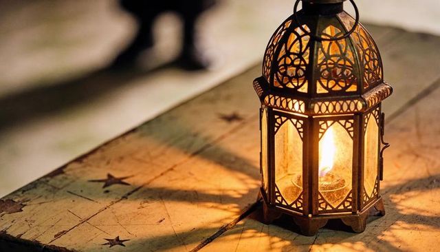 Ornate metal-glass lantern casting warm candlelight on worn star-pattern tabletop