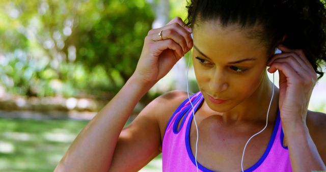 Woman is adjusting her earphones before engaging in outdoor exercise. She is wearing a sleeveless sports top and appears focused and ready for a workout. This image can be used for fitness blogs, exercise tutorials, sportswear advertisements, and wellness articles.