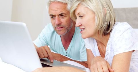 Senior Couple Relaxing in Bedroom Using Laptop Together