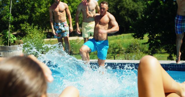 A group of people enjoys a sunny day by the pool, with a man in blue shorts jumping into the water, creating a splash. This lively scene captures the essence of summer fun and outdoor activities.