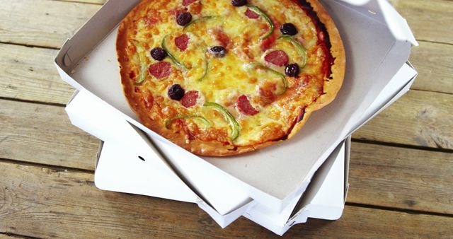 Appetizing pizza with cheese, pepperoni, bell peppers, and olives served in a delivery box on rustic wooden table. Ideal for representing food delivery services, takeaway restaurants, fast food promotions, or Italian cuisine.