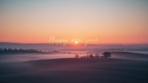 Golden sunrise over misty rolling hills with 'happy new year' script overlay