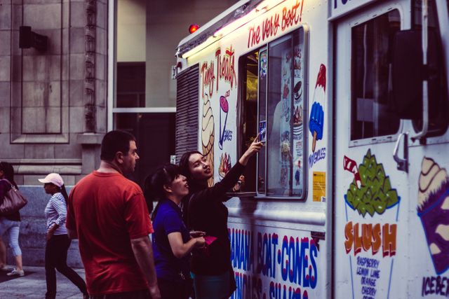 This image depicts a vibrant urban scene of people purchasing ice cream from a food truck on a city street. Ideal for illustrating urban lifestyle, street food culture or summer treats. Useful for travel blogs, urban life articles, food industry publications, and marketing materials related to leisure activities and outdoor events.