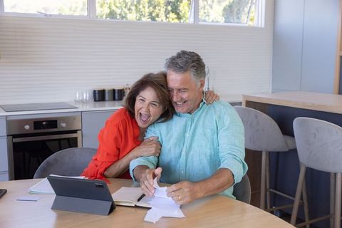 Senior couple celebrating good news while opening mail at modern kitchen table