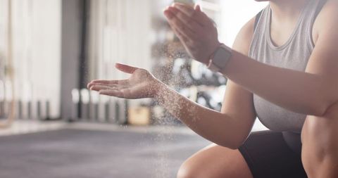 Female athlete applying chalk for grip wearing smartwatch in bright gym training scene
