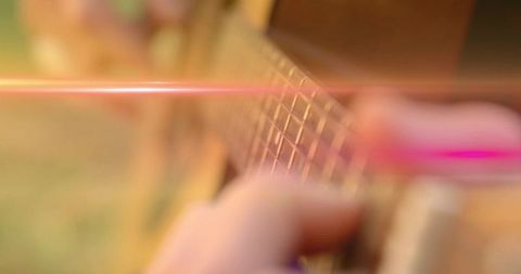 Close-up fretting hand pressing strings on acoustic guitar fretboard during golden hour