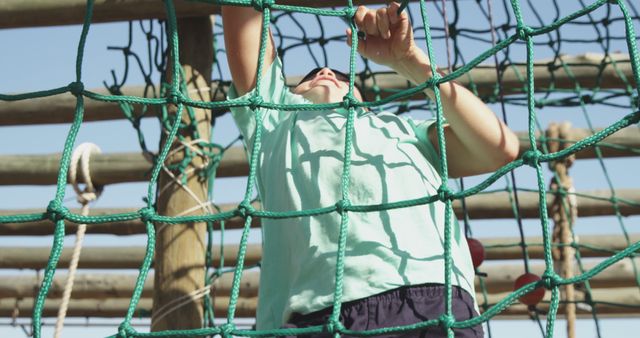 Boy is climbing rope nets in an outdoor adventure park, involved in physical challenge. Ideal for themes related to childhood, adventure, outdoor activities, strength, agility, summer camps, and sports. Perfect for use in advertisements, educational materials, and recreational promotions.