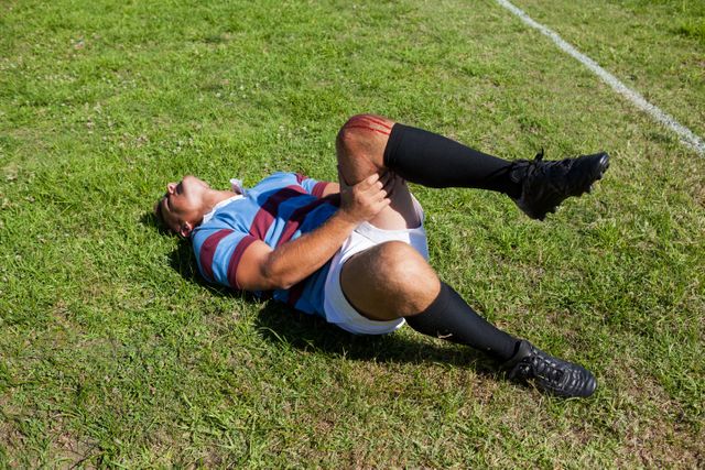 Full length of rugby player with injured knee lying on field during sunny day