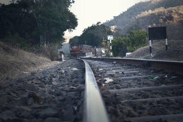 Close-up view of railway tracks extending into a distant train amidst a hilly and natural landscape. Ideal for themes related to transportation, travel, adventure, rail journeys, and nature. Useful for websites, blogs, or presentations focusing on railroad infrastructure, scenic travel routes, or railway industry.