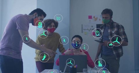 Masked team collaborating around laptop with ar energy, sustainability and analytics icons