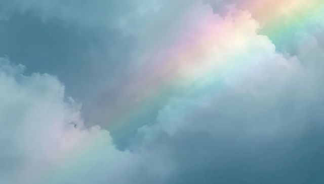 Pastel rainbow stretching through layered clouds, soft sunlight casting iridescent hues