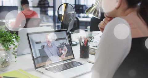 Woman watching virtual presentation on laptop in open-plan coworking office, focused productivity
