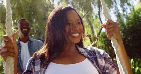 Joyful couple enjoying swing in sunlit garden