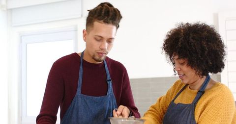 Couple Mixing Batter in Sunlit Modern Kitchen Wearing Denim Aprons and Smiling