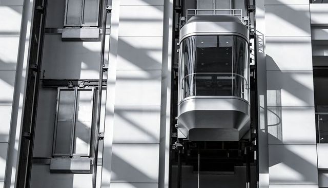Glass elevator cabin rising inside modern atrium casting bold geometric shadows