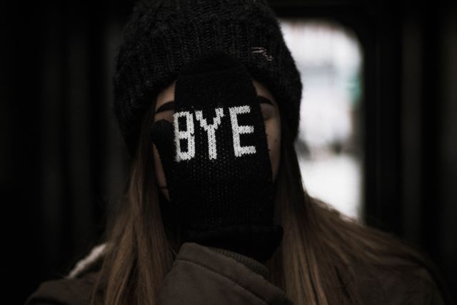Person wearing beanie and gloves showing 'BYE' text on hand in winter season. Ideal for topics like winter fashion, cold weather, casual attire, expressions, and winter activities.