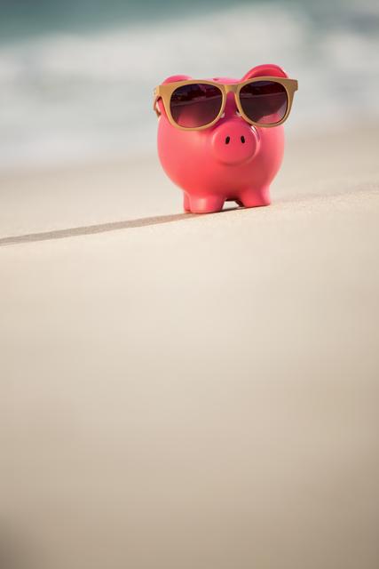 Summer piggy bank with sunglasses on sand at beach