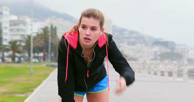 A young Caucasian female jogs along a scenic route, with copy space. Her focused expression and sporty attire suggest a commitment to fitness and an active lifestyle.