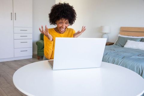 Excited Woman Celebrating Success with Laptop in Modern Bedroom