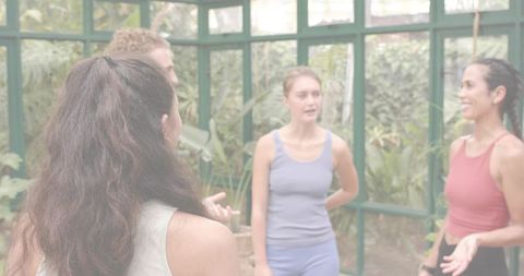 Fitness instructor leading small group workout in sunlit conservatory with tropical plants
