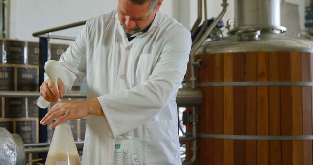 Craft brewer inspects beer sample with a beaker in a microbrewery. Useful for articles on craft beer production, fermentation process, quality control in breweries, and the works of a brewer.