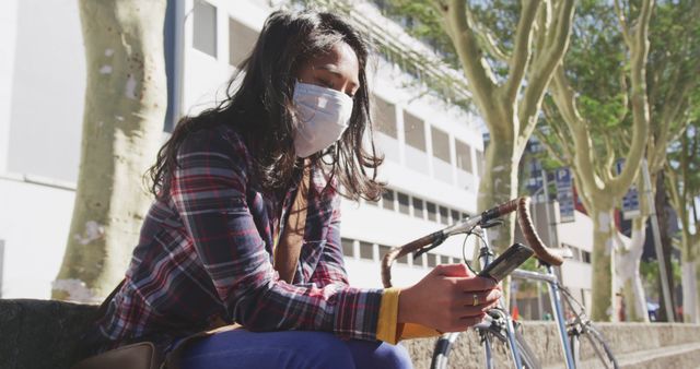 Masked Woman Using Smartphone in Urban Park with Bicycle Nearby - Download Free Stock Images Pikwizard.com