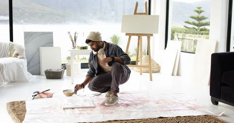 Indian man creating large abstract painting on floor in bright coastal home studio