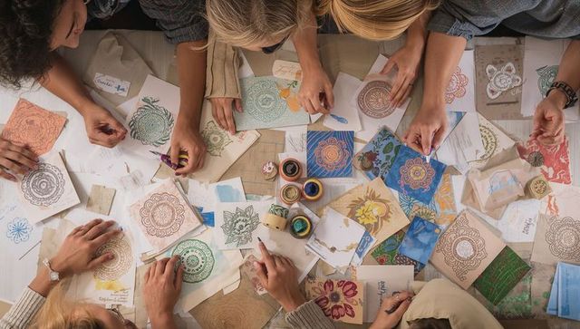 Craft workshop hands creating colorful mandala prints on papers and cards overhead