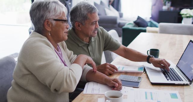 Senior biracial couple talking and using laptop. Spending quality time at home, retirement and lifestyle concept.